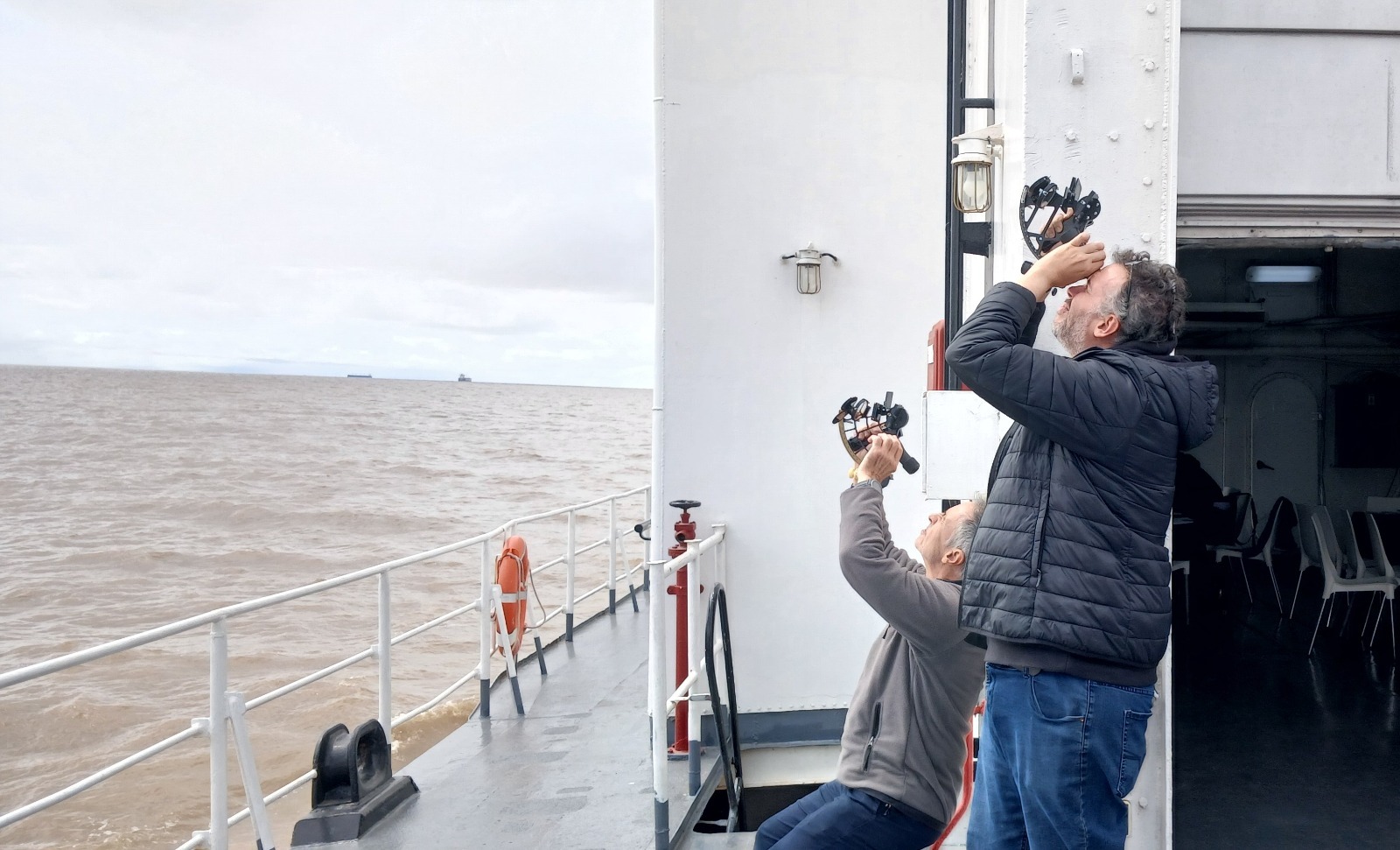 Dos adultos practican navegación astronómica con sextantes a bordo de una embarcación, en una fotografía difundida por Prefectura para su curso de Piloto de Yate 2027. Fecha de toma no informada.