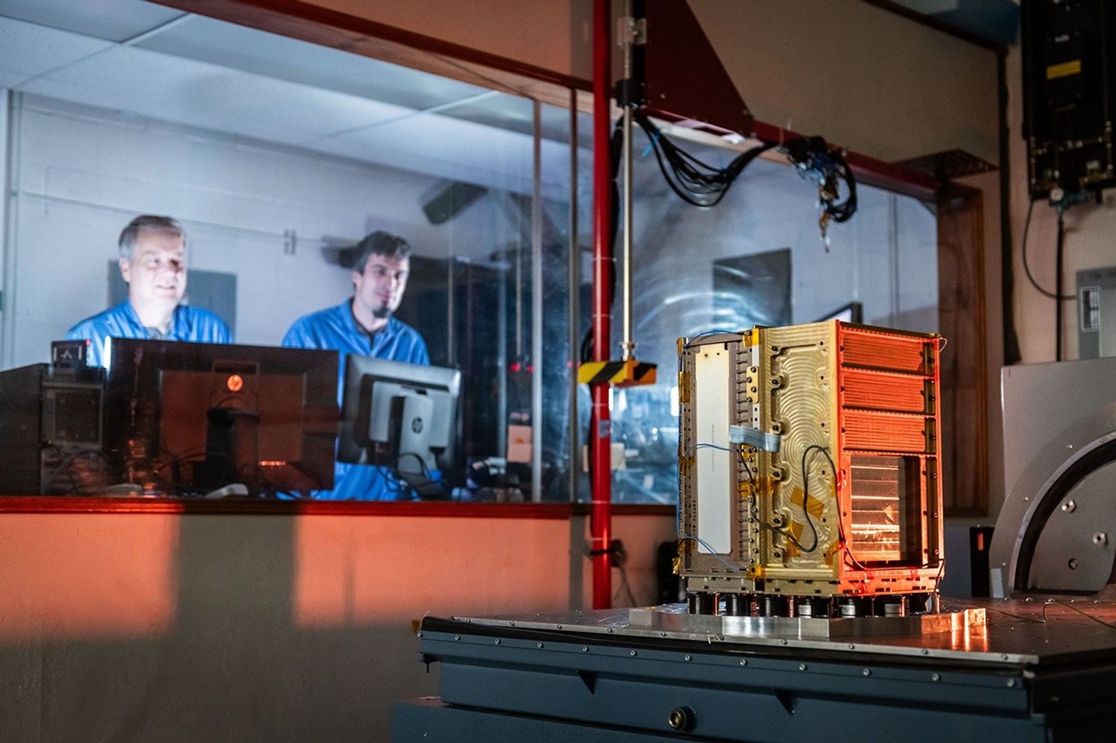 Dos ingenieros observan una prueba de vibraciones de un satélite SunRISE en el Space Dynamics Laboratory; fotografía de archivo de octubre de 2025.