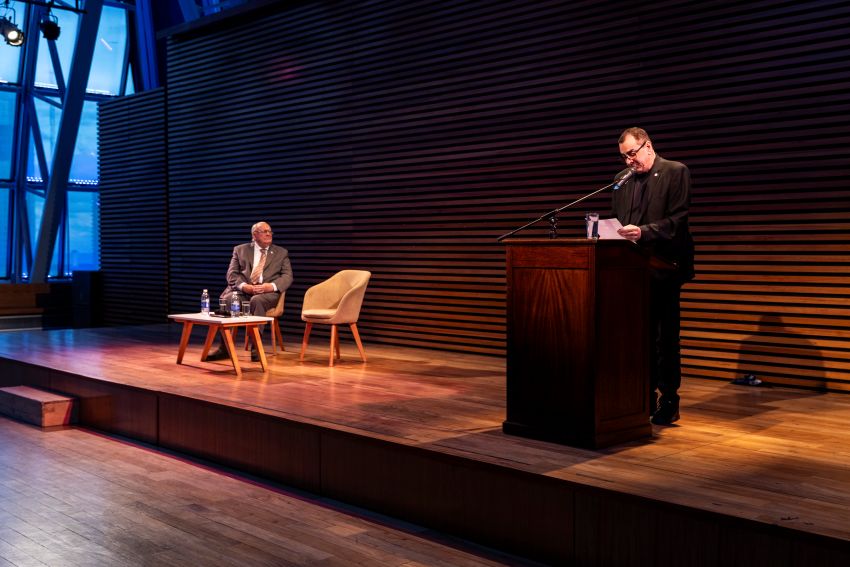 Pedro Luis Barcia sentado en el escenario y Leonardo Cifelli en el atril durante el reconocimiento del 26 de octubre de 2026 en el Palacio Libertad.