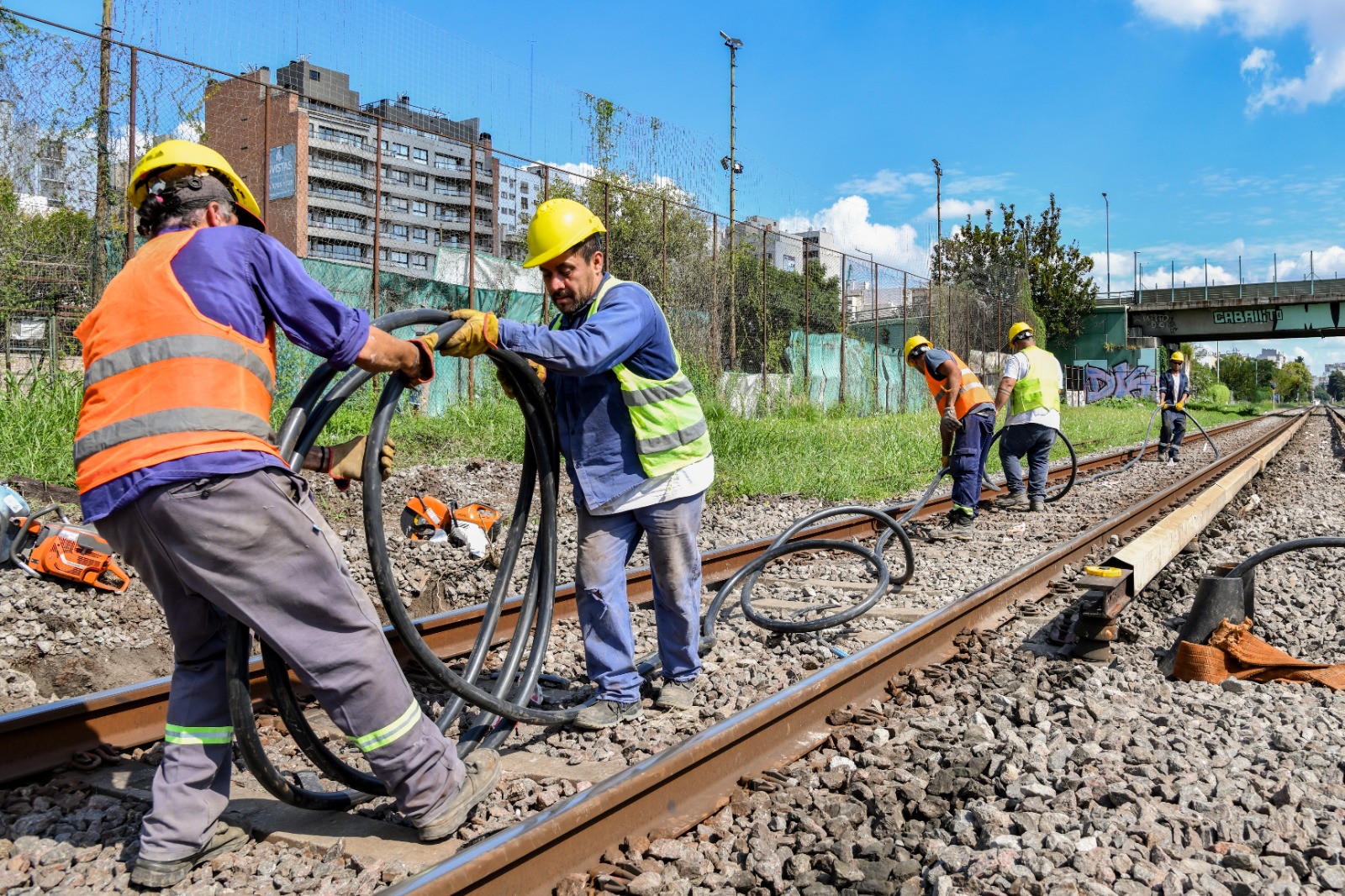 Trabajadores con cascos y chalecos manipulan cables junto a las vías del Sarmiento, en una imagen difundida con el anuncio oficial.
