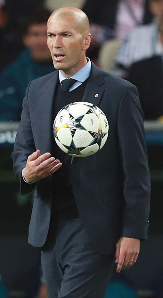Foto de archivo de 2018: Zinedine Zidane, de traje, sostiene una pelota junto al campo de juego.