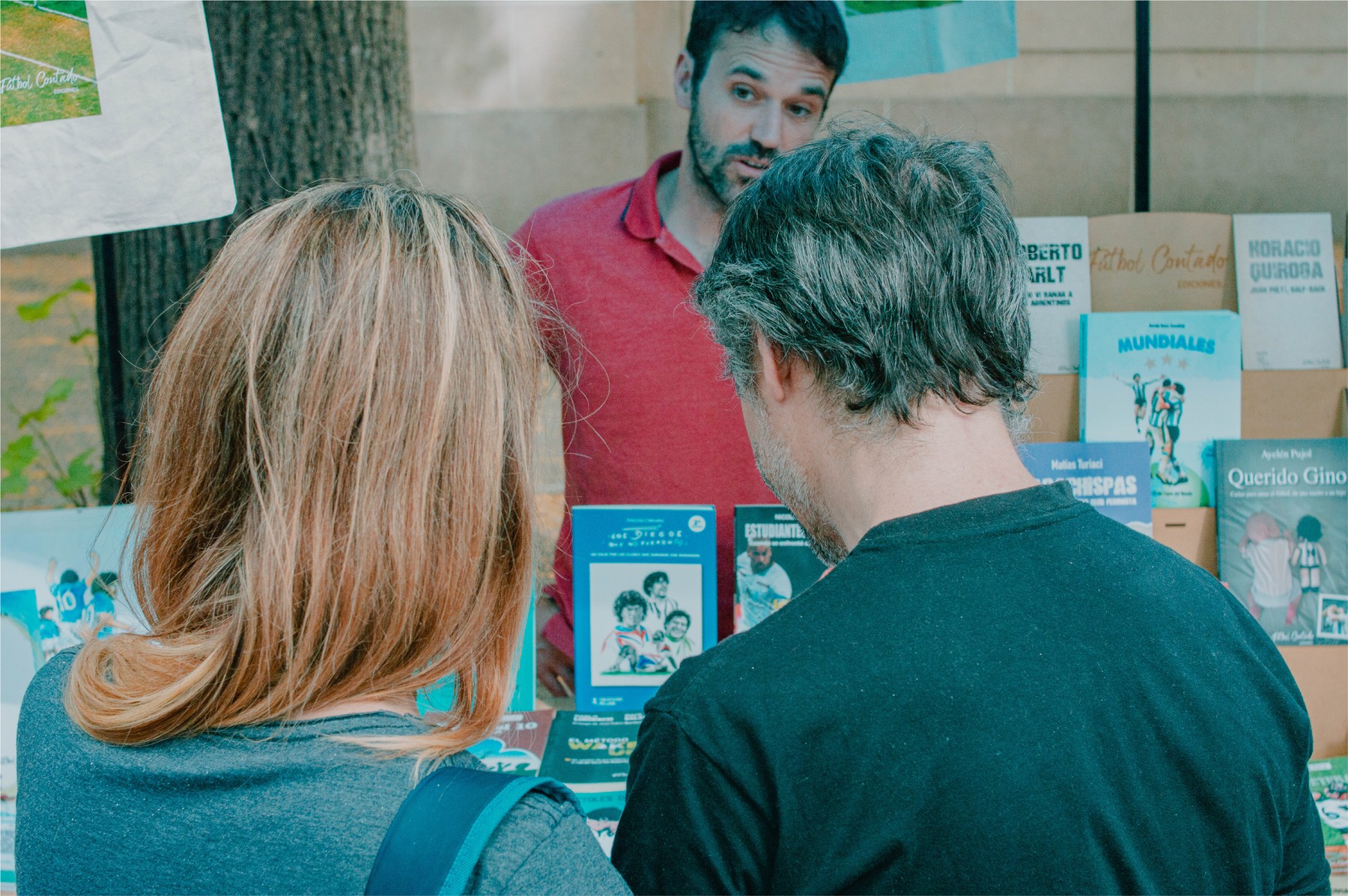 Visitantes adultos conversan con un expositor junto a los libros de un puesto de la Feria EDITA en La Plata. Foto de archivo difundida por la organización.