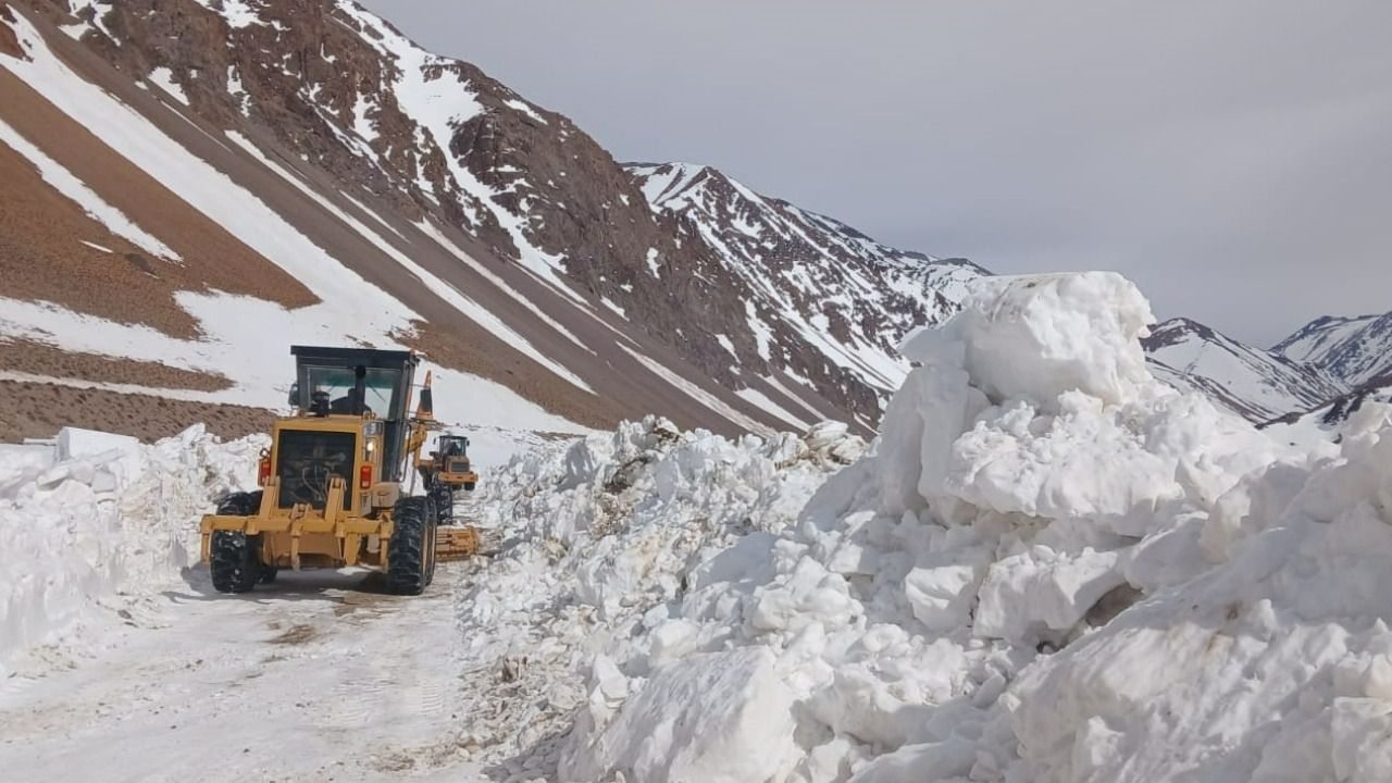 Una máquina vial trabaja junto a una pared de nieve en un camino cordillerano.