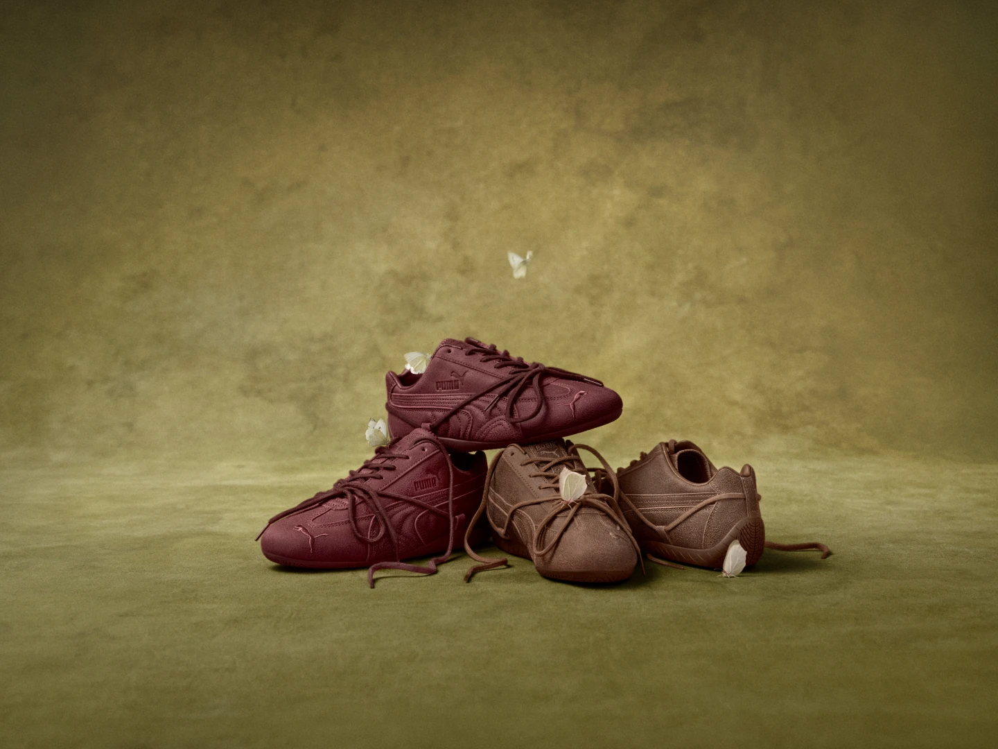 Dos pares de Puma x Rosé Speedcat, en tonos marrón y borgoña, sobre una superficie verde con flores. Fotografía del lanzamiento difundido el 5 de octubre de 2026; fecha de toma no informada.