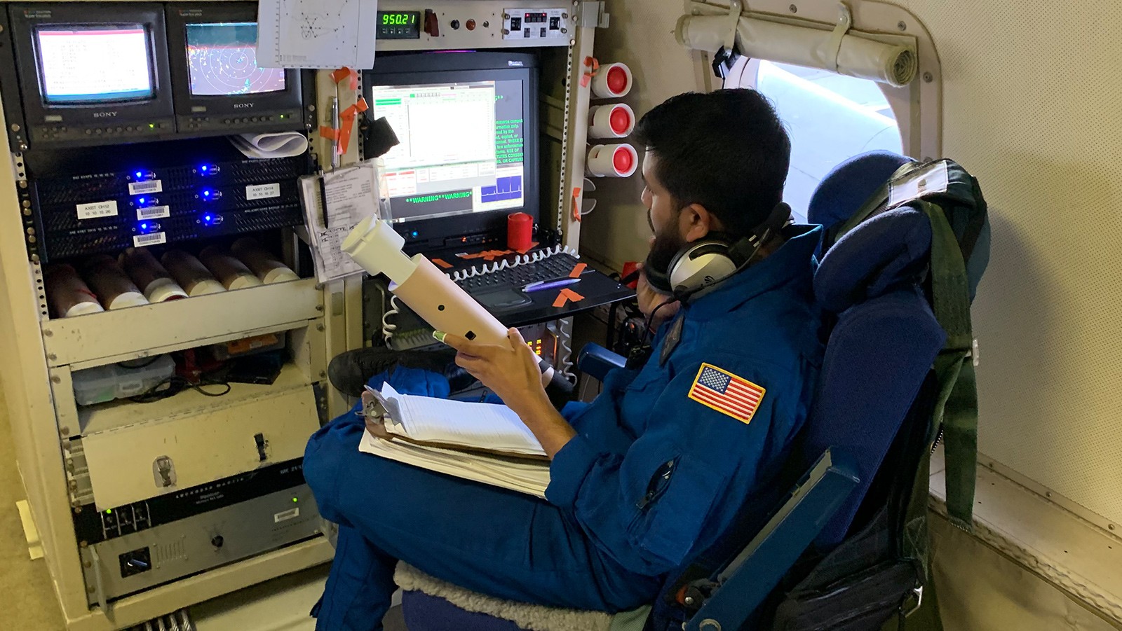 Investigador de NOAA con una sonda atmosférica junto a equipos de medición dentro de un avión. Fotografía de archivo; fecha de toma no informada.