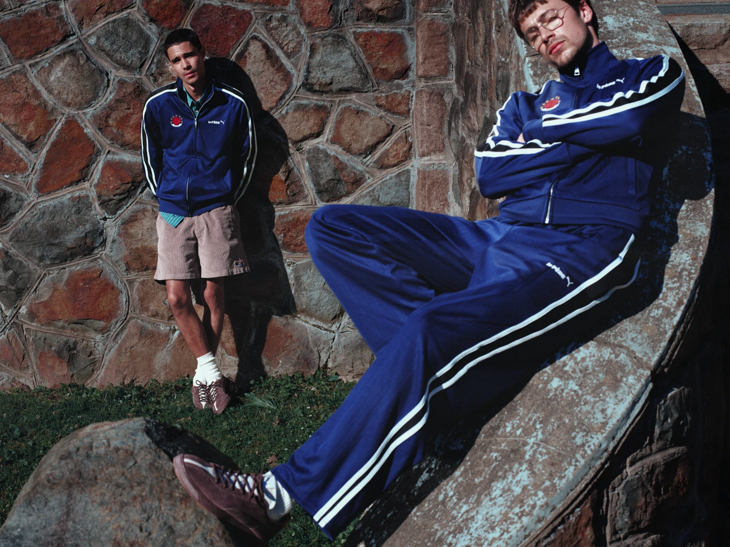 Luca Apple y Jeff Wahlberg visten conjuntos y calzado Puma x le PÈRE, junto a una pared y una estructura de piedra. Fotografía de la campaña difundida el 6 de octubre de 2026; fecha de toma no informada.