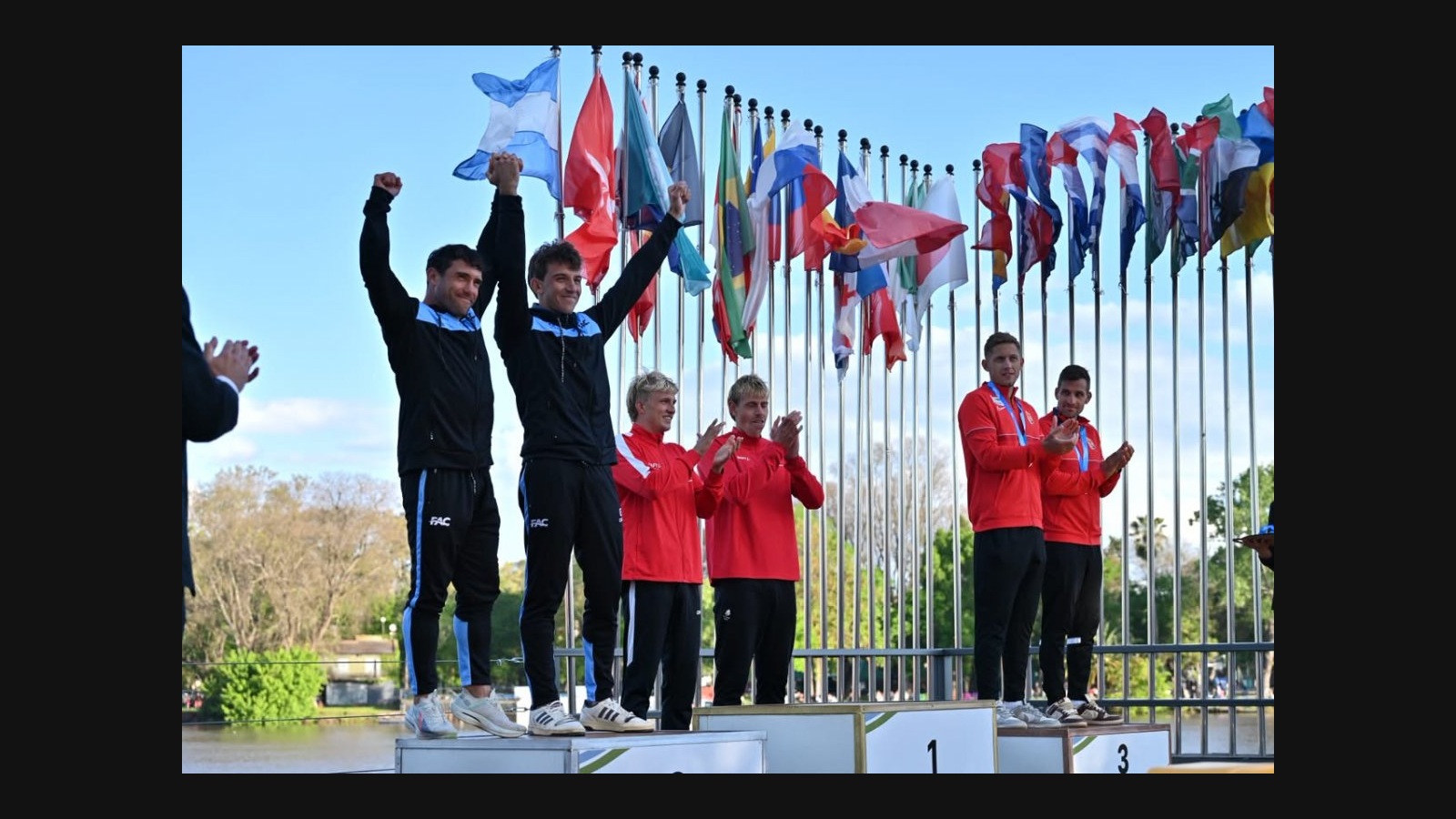 Ratto y Cáceres levantan los brazos en el segundo escalón del podio del K2 masculino sénior en Gualeguaychú, junto a las duplas de Dinamarca y Hungría.