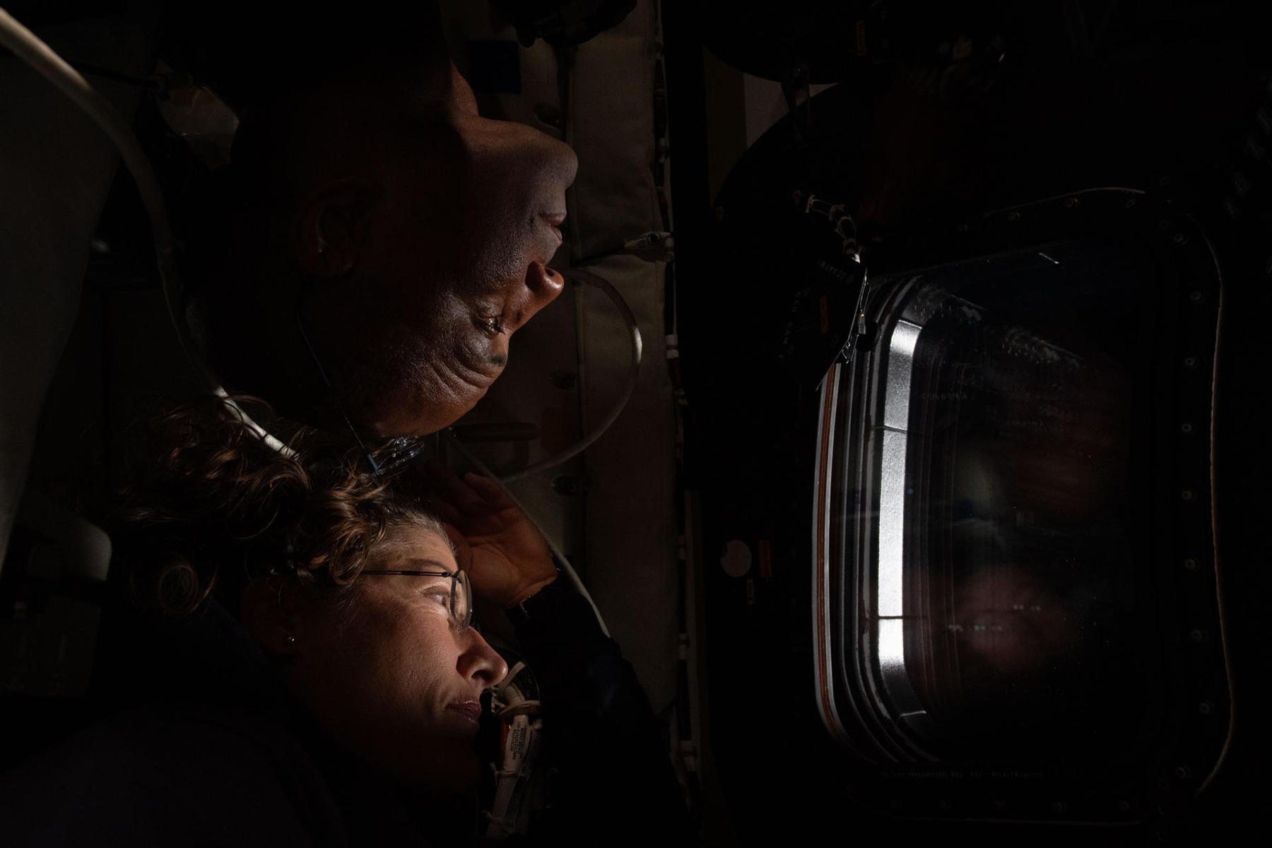 Victor Glover, arriba y cabeza abajo, y Christina Koch, debajo, observan por una ventana de Orion. Archivo del sobrevuelo lunar de Artemis II, 6 de abril de 2026.